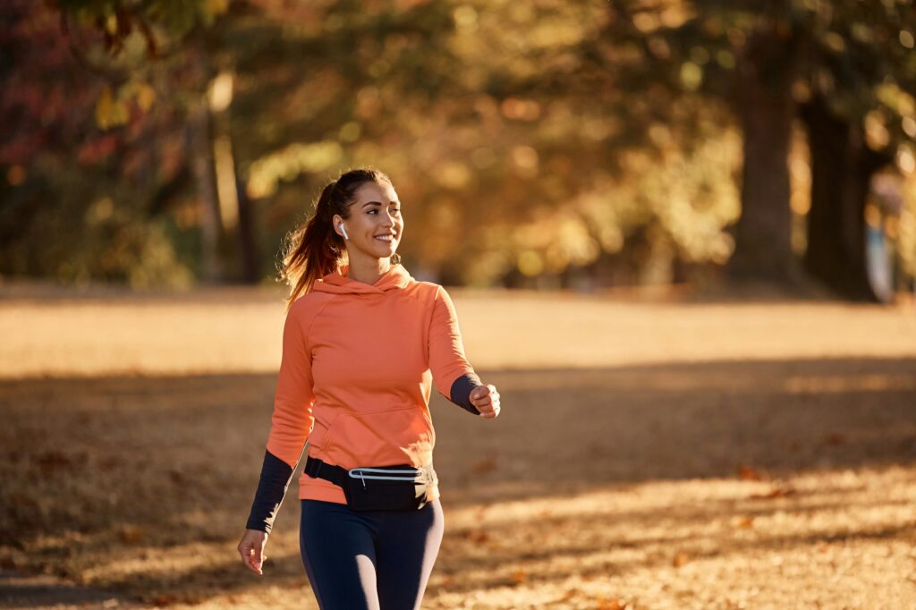 Happy sportswoman enjoying while walking in nature during autumn day.