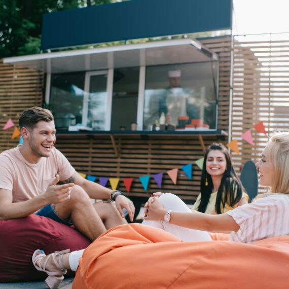 happy young friends talking while sitting on bean bag chairs near food truck