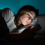 Woman using mobile phone while lying in bed at night, suffering from post-breakup insomnia. Anxiety.