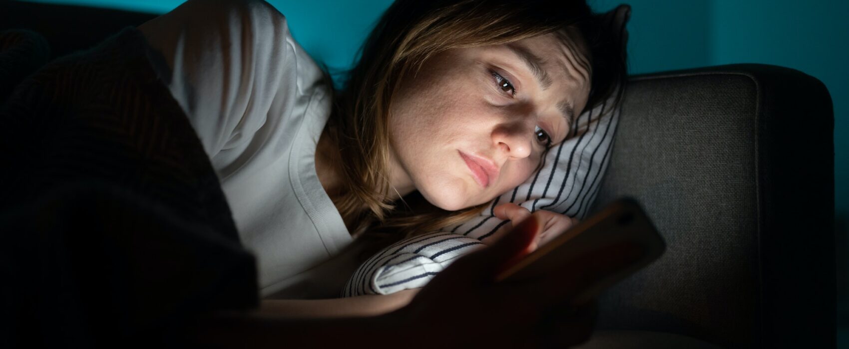 Woman using mobile phone while lying in bed at night, suffering from post-breakup insomnia. Anxiety.