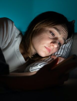 Woman using mobile phone while lying in bed at night, suffering from post-breakup insomnia. Anxiety.