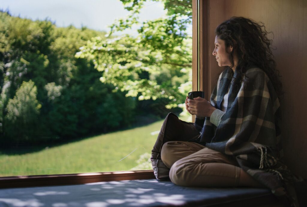 Woman with coffee sitting indoors in a tree house, weekend away and digital detox concept.