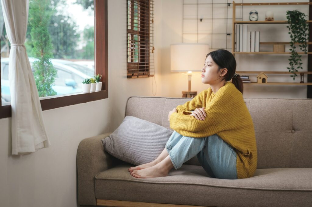 Young Asian woman suffering from work stress sits alone on the sofa at home discouraged. Desperate A