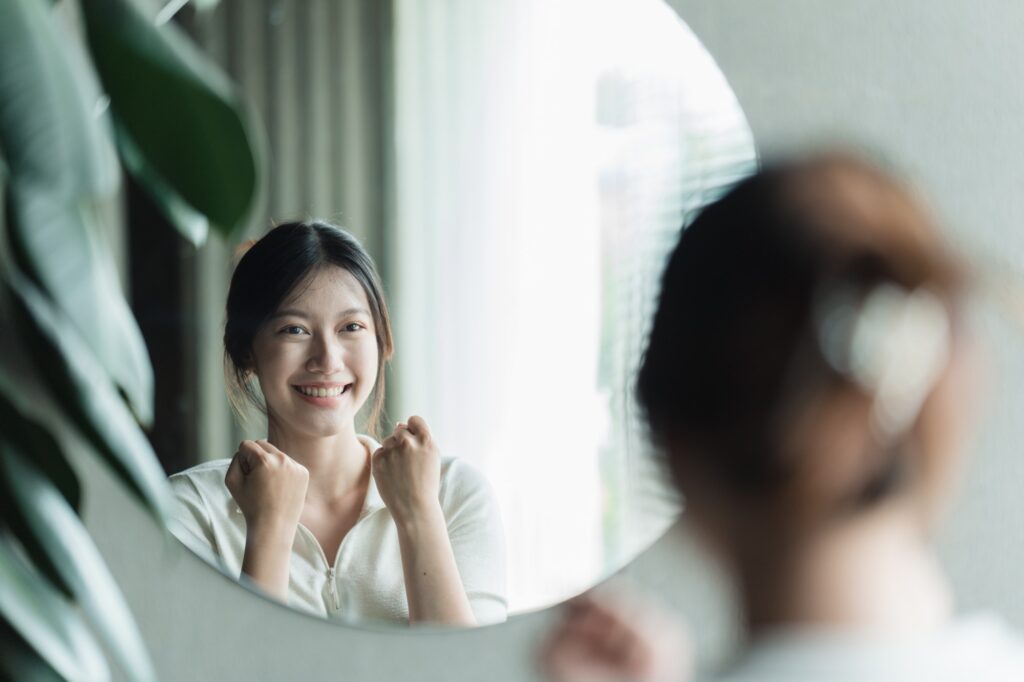 A young Asian woman talks to herself through a mirror to build her self-confidence and empower herse