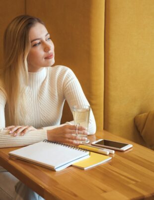 Beautiful young girl student sitting by the window in university cafe and waiting someone