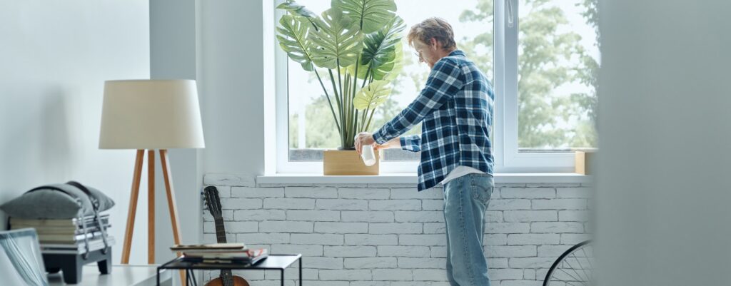 Confident young man watering his plant at home