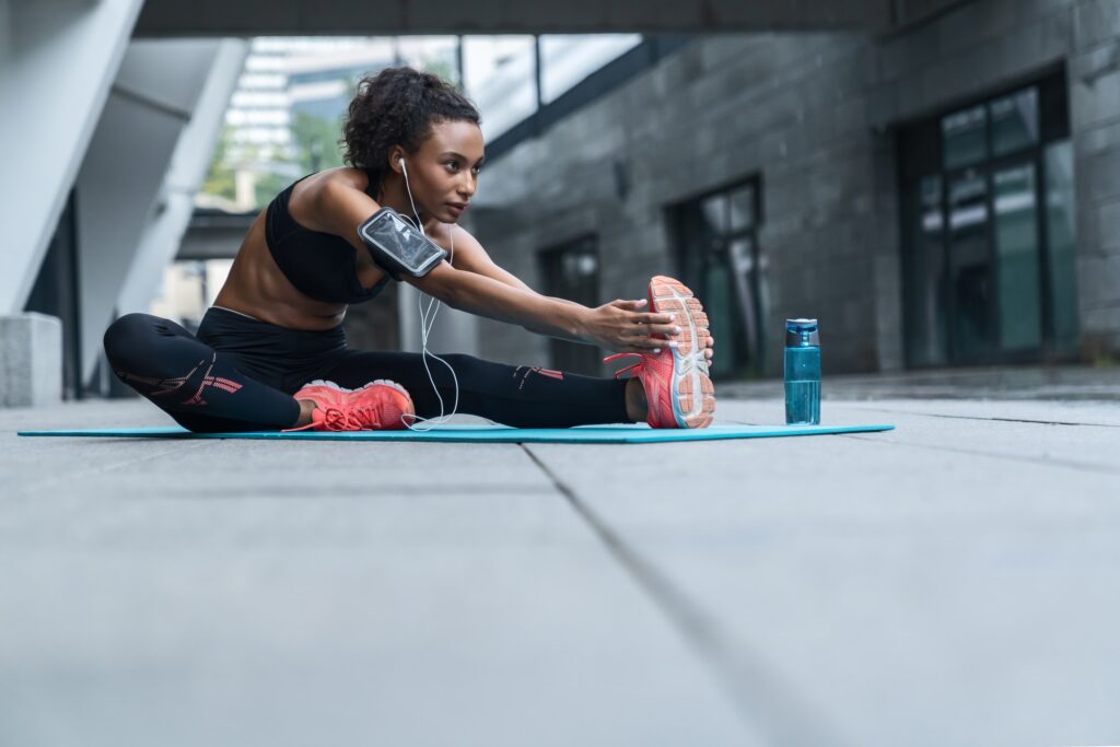 Fitness woman with earphones exercising and stretching outdoors on fitness mat