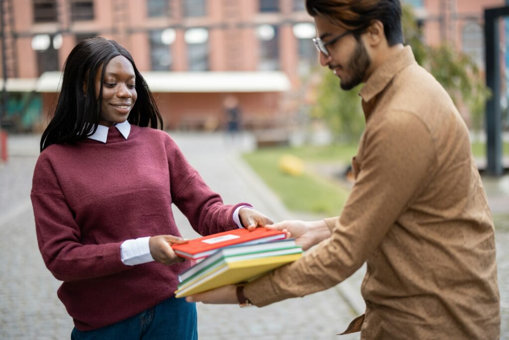 Indian man giving books to black girl outdoors