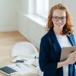 Prosperous female leader of working team holds digital tablet device, develops business ideas