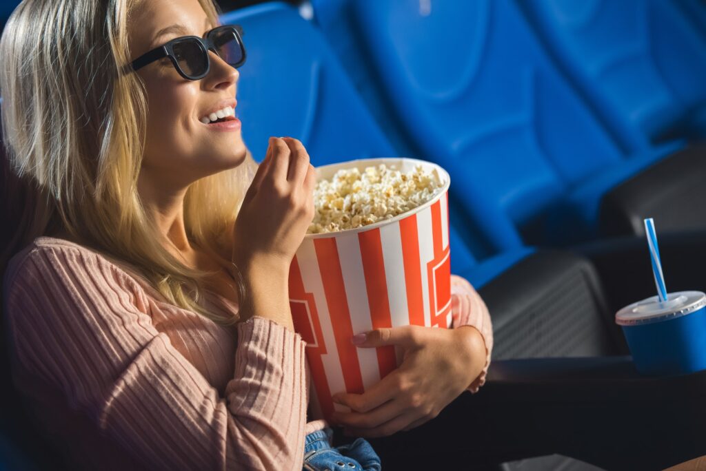 side view of smiling woman in 3d glasses with popcorn watching film alone in cinema