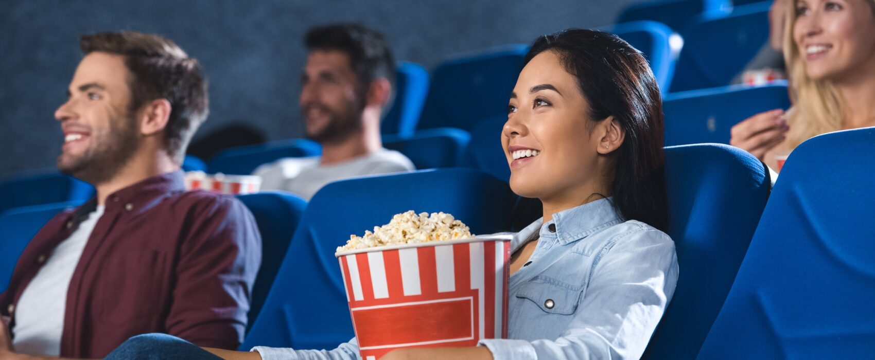 smiling asian woman with popcorn watching movie in cinema alone