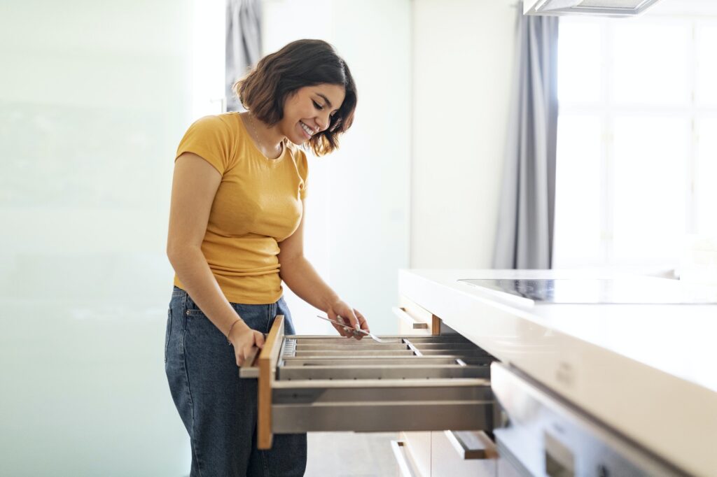 Young arab woman tidying up cutlery in drawer while cleaning in kitchen