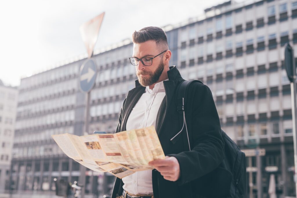 Young caucasian bearded man outdoors getting lost using guide map