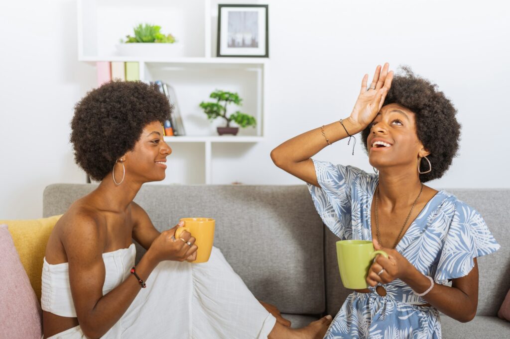 Black twin sisters, drinking a cup of coffee, having a happy and expressive conversation