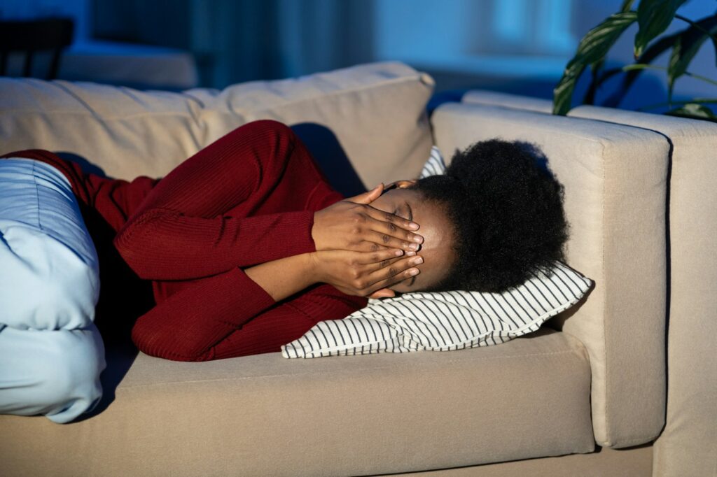 Depressed african woman lying on sofa crying alone at home, suffering from bad toxic relationship