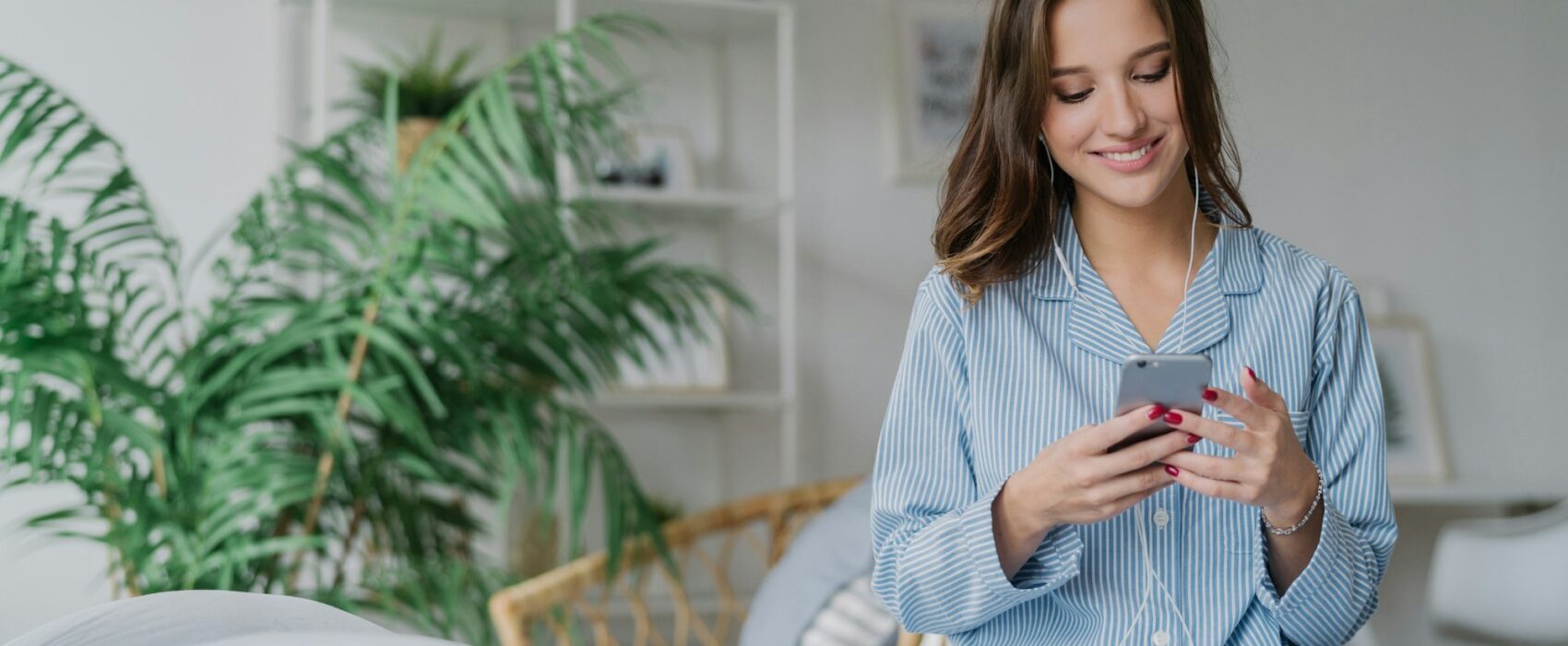 Happy woman with appealing look, holds modern cell phone, downloads song to playlist