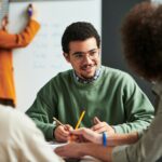 Happy young man in eyeglasses communicating with another student