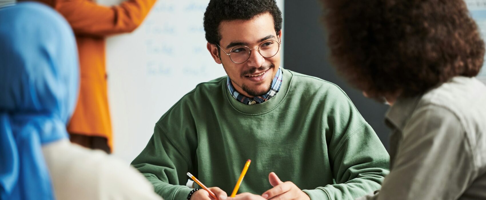 Happy young man in eyeglasses communicating with another student