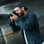 Photography hobby. Young stylish man standing on city street taking photos on camera concentrated