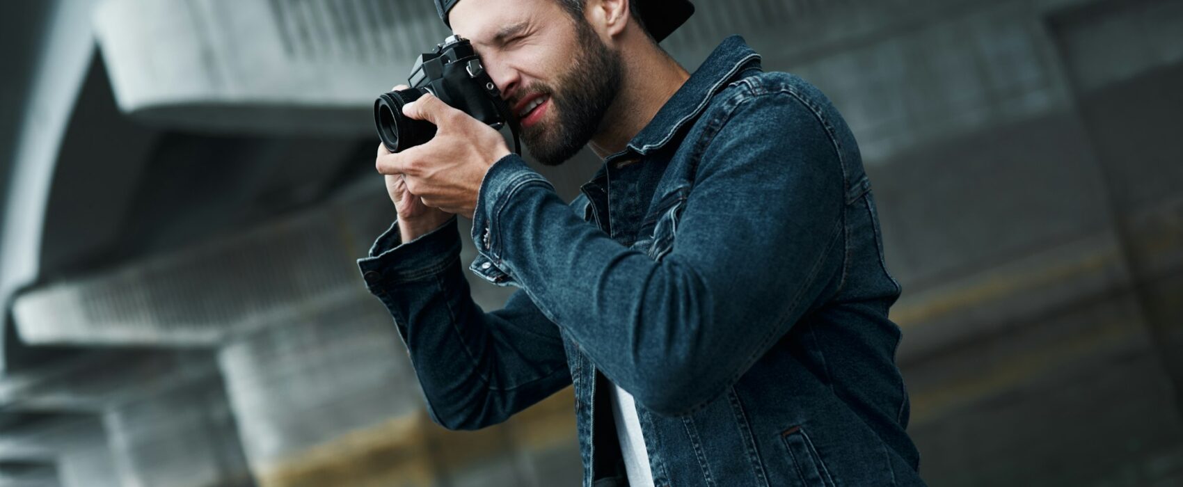 Photography hobby. Young stylish man standing on city street taking photos on camera concentrated