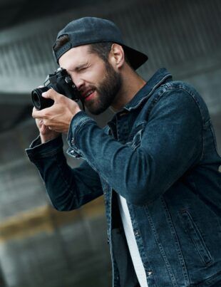 Photography hobby. Young stylish man standing on city street taking photos on camera concentrated