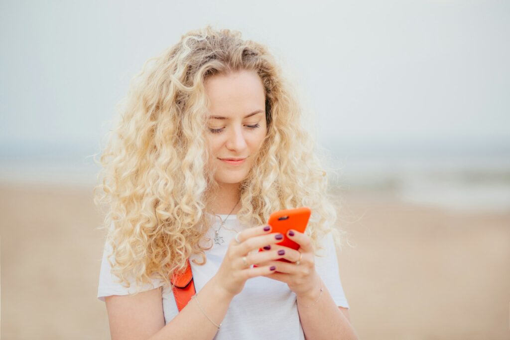 Pleasant looking curly female uses modern cell phone for online communication, being always in touch