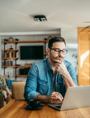 Portrait of a casual businessman thinking while looking at laptop screen, keeping hand on chin.