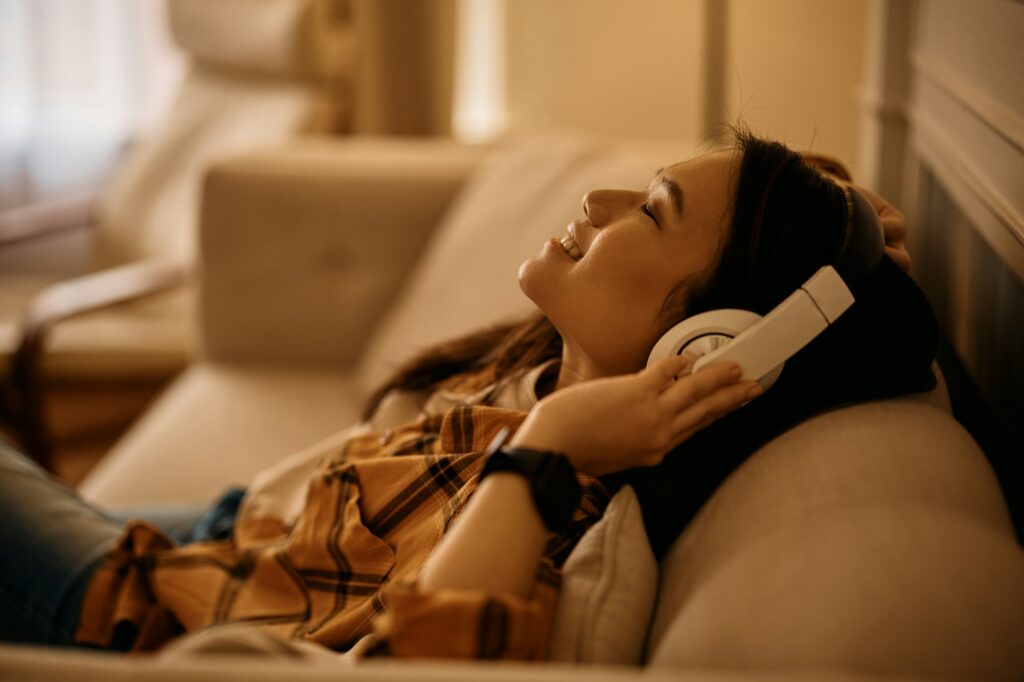 Relaxed Asian woman enjoying in music over headphones at home.