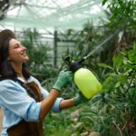 Young woman gardener caring plants treating flowers with chemicals