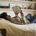 Young woman lying on bed reading a book