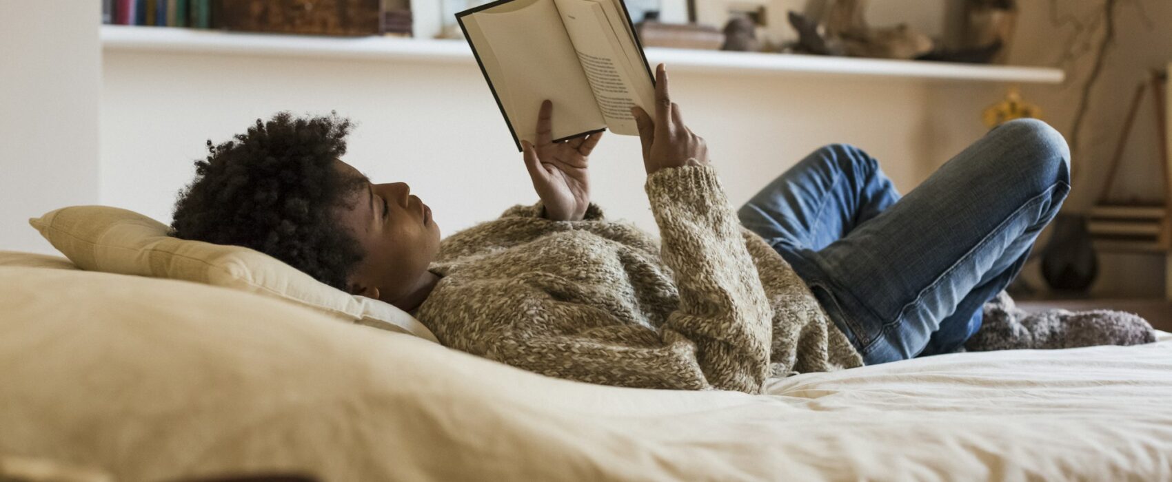 Young woman lying on bed reading a book