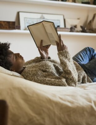 Young woman lying on bed reading a book