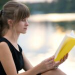 Young woman resting in summer park reading a book. Education and sudy concept