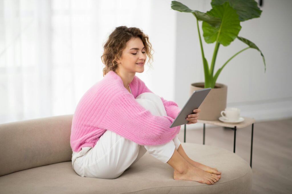 Smiling young woman relaxing with digital tablet on couch at home