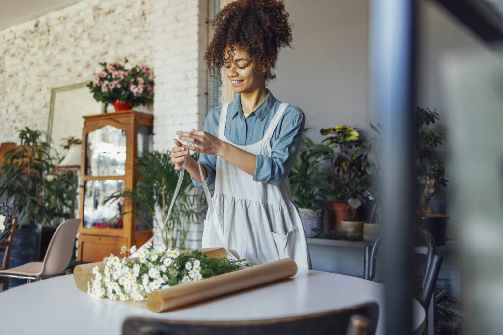 Young florist in apron creating beautiful simple daisy bouquet in craft paper