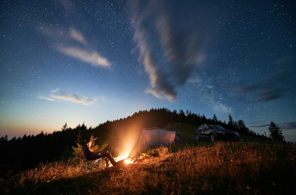 Young man relaxing next to bonfire on hill.