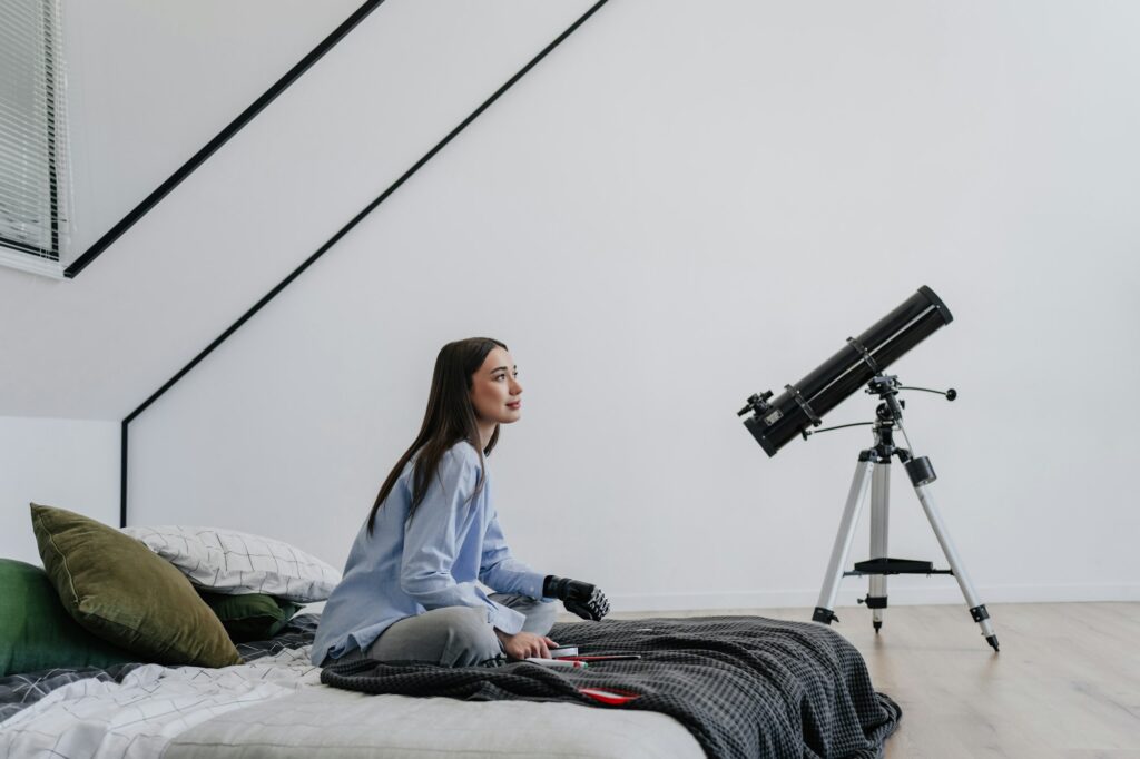 Young woman with artificial bionic hand with a telescope indoors, looking curious and contemplative